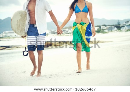 Brasil latino hispanic couple walking holding hands with surfboard and flag as sarong