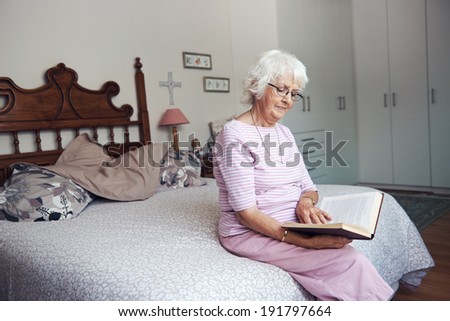 An old woman sitting on her bed reading a book with copyspace