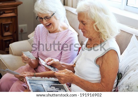Two old women looking at old photographs together and laughing