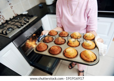 Cropped image holding a tray of home baked muffins just out of the oven in the kitchen