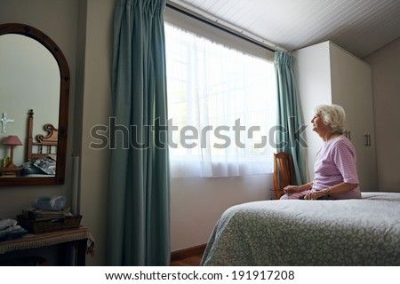 A depressed elderly widow sitting on her bed looking out the window