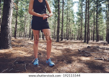 Woman runner checking pace on gps sports watch in forest