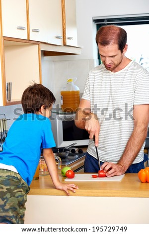 Dad chopping tomato in kitchen as young son watches