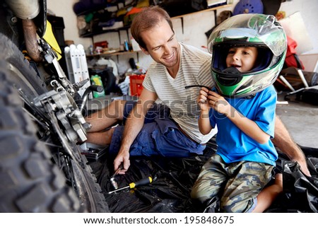 portrait of young boy playing with fathers motorbike helmet and helping his dad with fixing a motorcycle in the garage