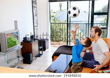 Father and son watching football world cup soccer on tv together in living room on sofa being excited fans