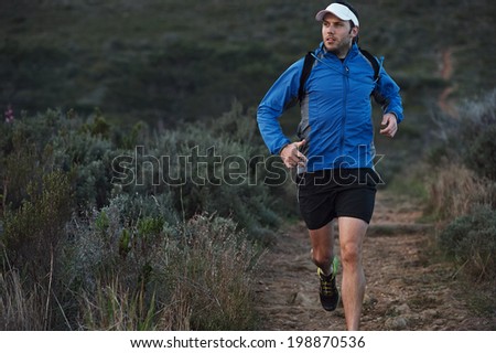 ultra marathon trail runner training in mountains for fitness and exercise wearing windbreaker
