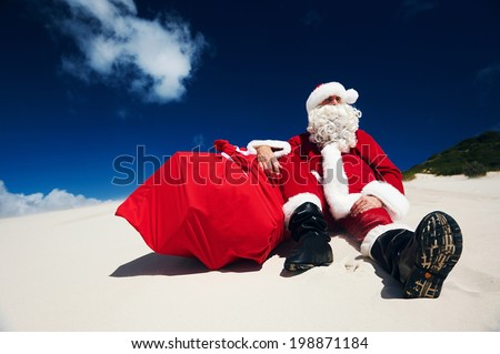 Father Christmas sitting on the beach sand next to his sack of presents