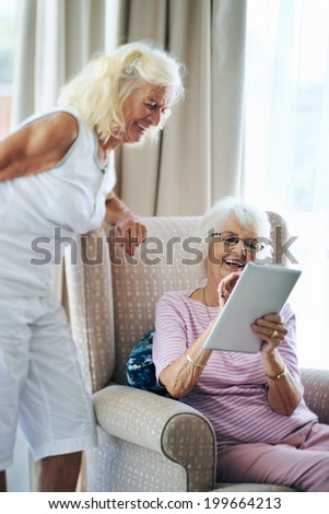 Happy old female friends laughing together and looking at touchscreen