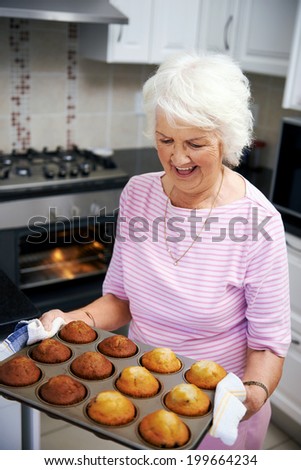 Happy old lady taking muffins out of the oven