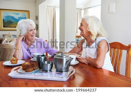 Two retired older women sitting together having tea and muffins and laughing