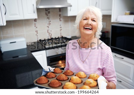 A laughing pensioner holding a tray of baked muffins just out of the oven