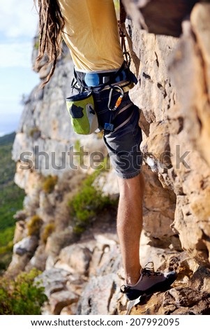 Cropped image of a man with dreadlocks finding a foothold on a steep mountain
