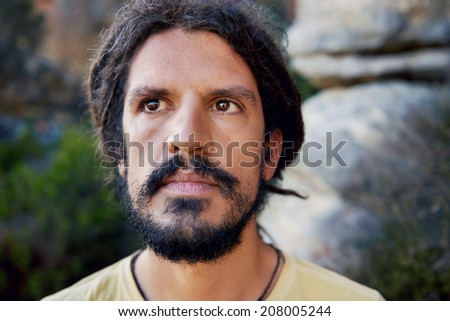 A man with dreadlocks looking off camera in natural background