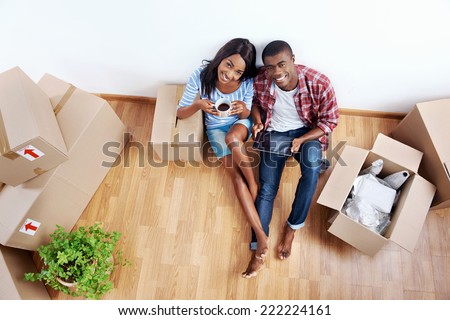 overhead view of young black african couple with moving boxes in new apartment using modern tablet computer technology