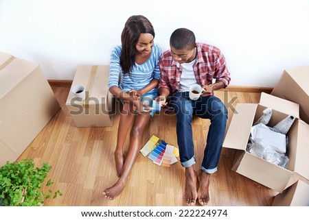 overhead view of young black african couple with moving boxes in new apartment choosing colour of paint for walls