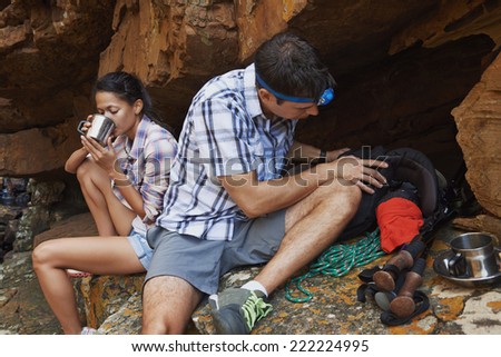 A hiking couple taking a break by a cave with their hiking utensils around them