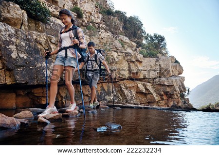 An attractive hiking couple balancing on rocks to get across the water with copyspace