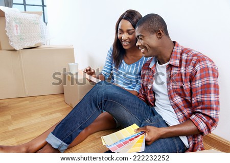 young african couple having fun deciding on paint colour swatch for new home apartment