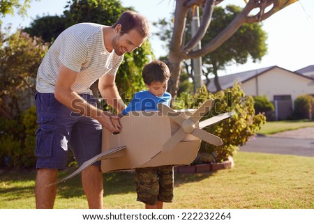 son and dad playing with toy aeroplane in the garden at home having fun together and smiling