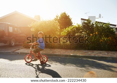 young boy learning to ride bicycle with training wheels at sunset
