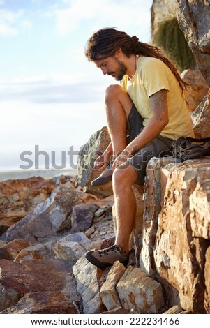 Hiker with dreadlocks tying his shoelaces on a mountain