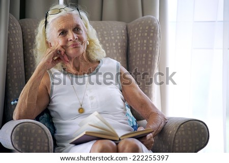 A content elderly woman sitting on her sofa with a book in her lap