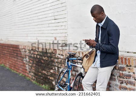Hipster man with bicycle sending message on mobile cell phone in urban city