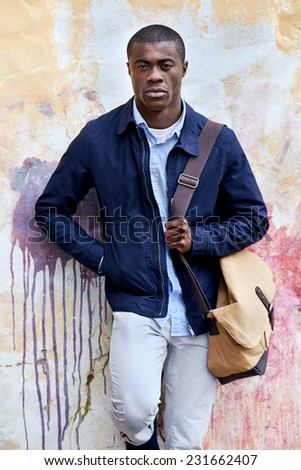 fashionable african hipster man portrait leaning against distressed urban wall background