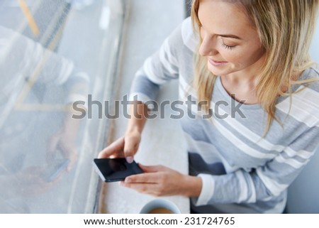 young woman chatting on phone while standing at the window and drinking coffee