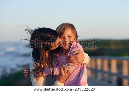 Unconditional love between mother and daughter hugging and embrace with a kiss and cuddle outdoors having fun