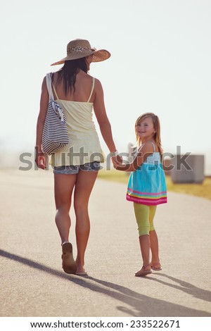 Mother and Daughter walking together at the beach holding hands in summer