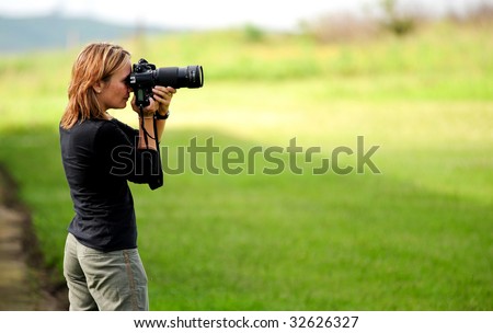 A woman frames a shot using her SLR digital camera. she steadies the professional camera with both hands because her lens is both long and heavy.