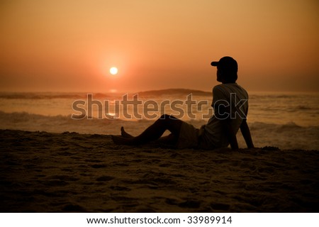 A man with a cap watches the sun as it moves on the horizon.