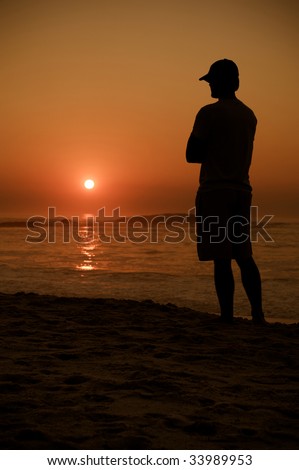 Man with cap watches the setting sun over the ocean