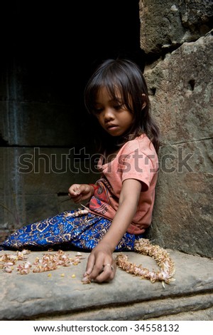 SIEM REAP, CAMBODIA - CIRCA JANUARY 2009: A young unidentified girl makes a souvenir necklace at Angkor Wat temple circa January 2009 in Siem Reap, Cambodia. Allegedly, children help to support their families.