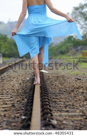 Girl in blue dress walks along the tracks on a summer day