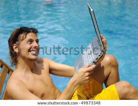 Attractive man uses his laptop while tanning poolside