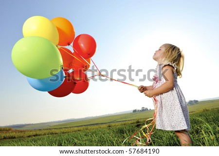 Adorable young girl holds tightly to a large bunch of helium filled balloons
