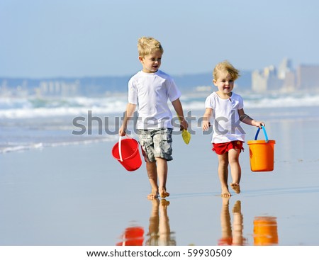 Brother and sister walk along the ocean edge looking for shells