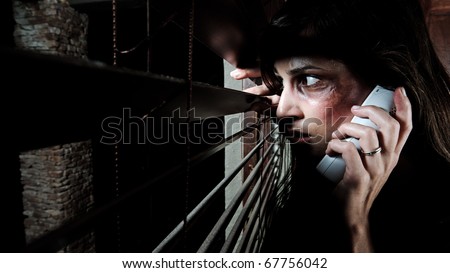 Fearful battered woman peeking through the blinds to see if her husband is home while calling for help