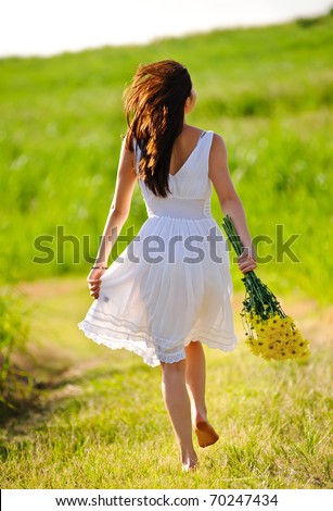 White dress skipping girl in field with flowers at sunset