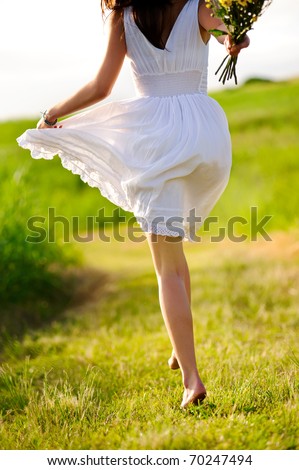White dress skipping girl in field with flowers at sunset