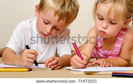 two adorable happy children drawing with crayons at playschool