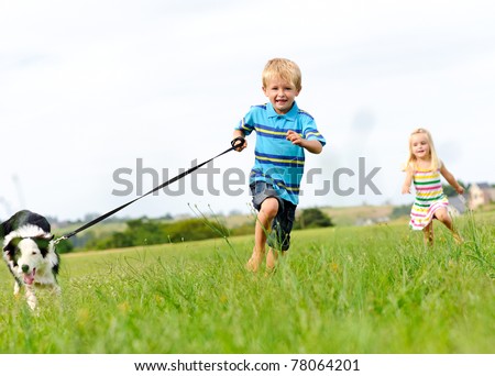 Young boy runs in a green field with his new pet with his sister following behind