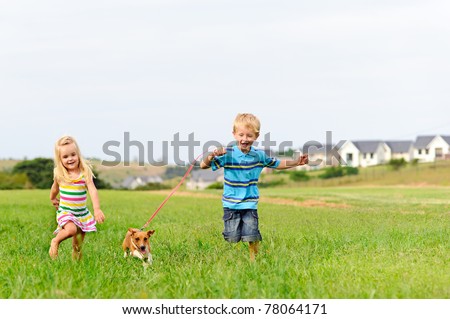 Brother and sister runs in a green field with their new pet