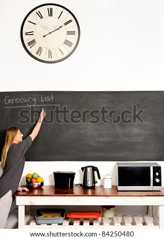 Young blond woman stretches out to write on a blackboard in the kitchen