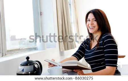 Pretty woman relaxes at home by the window with her tea and book