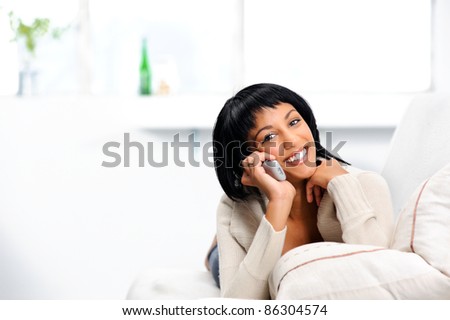 Attractive indian woman at home, lying on the couch with a telephone