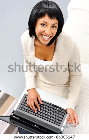 Top down perspective of a cute indian woman holding a credit card and typing on a laptop