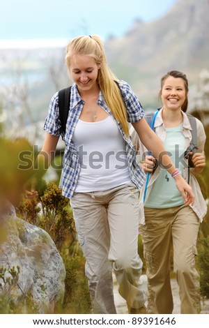 two young woman go hiking outdoors and smile as they walk